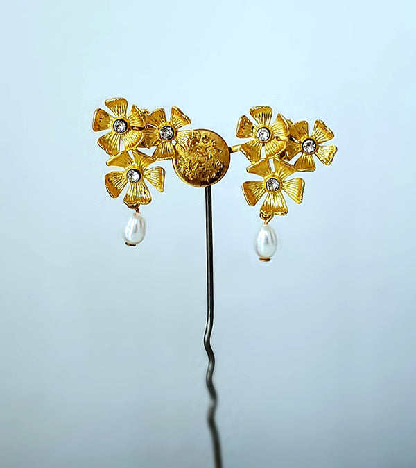 Des boucles d'oreilles percées composées de trois petites fleurs à 5 pétales, gravées comme de petits soleils dorés. En papille, une petite perle d'eau douce.