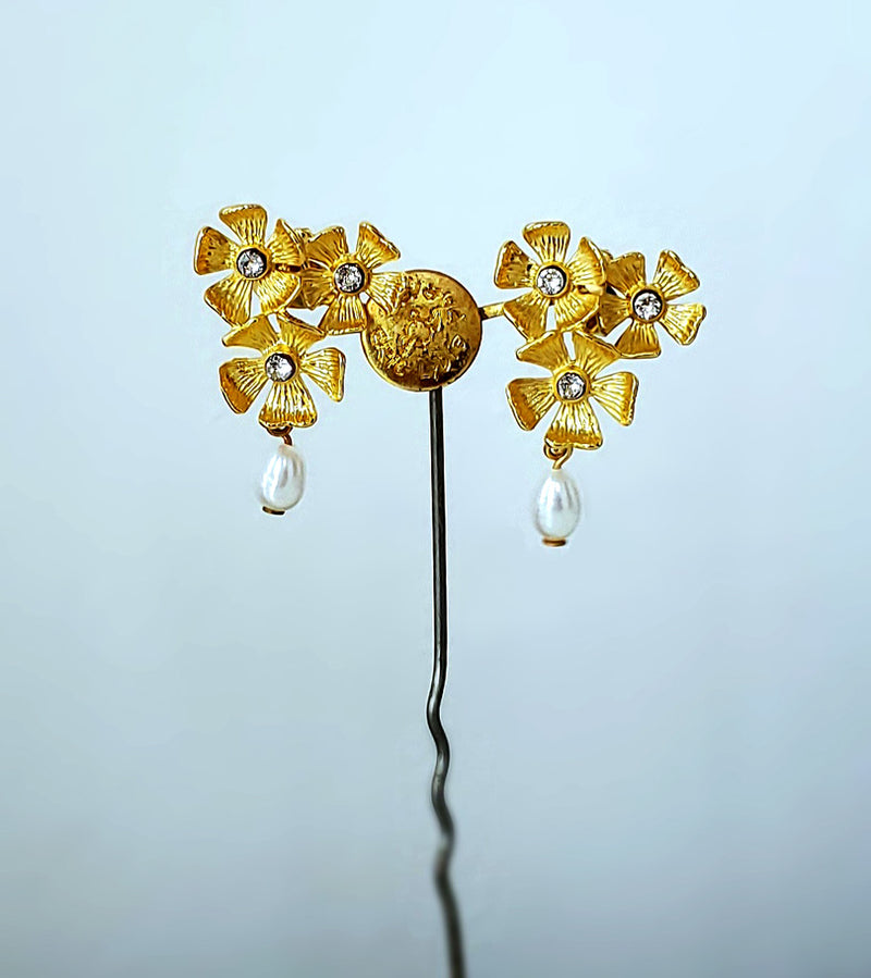 Des boucles d'oreilles percées composées de trois petites fleurs à 5 pétales, gravées comme de petits soleils dorés. En papille, une petite perle d'eau douce.
