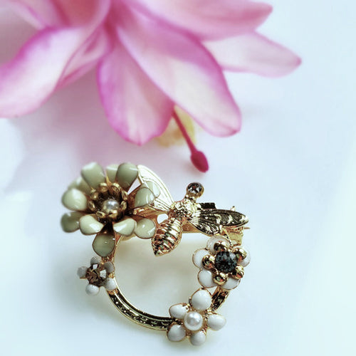 broche  printanière émaillée, une abeille butinant les fleurs. Coloris blanc. strass Swarovski.
