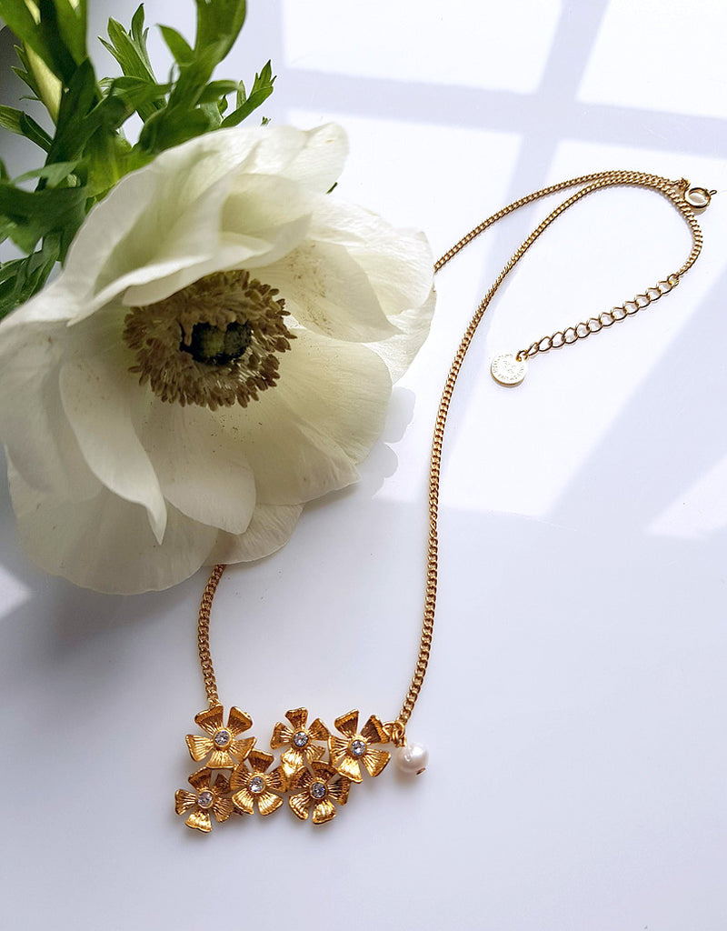 un collier tour de cou composé de 6 petites fleurs gravées, dorées à l'or fin, qui éclatent comme de petits soleils. Au coeur de chaque fleur un petit cristal Swarovski. Une petite perle d'eau douce en pendant sur le côté.