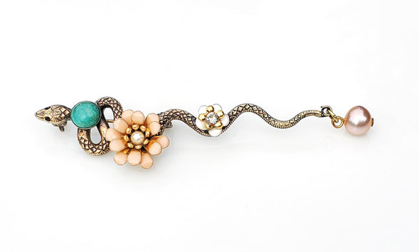 Broche serpent en métal bronze patiné. le long de son corps sont posés un cabochon en pierre amazonite, une fleur pompon en émail époxy rose nude, une petite fleur en émail blanc et un cristal Swarovski, une perle d'eau douce rose en pampille au bout de la queue de cet élégant serpent.